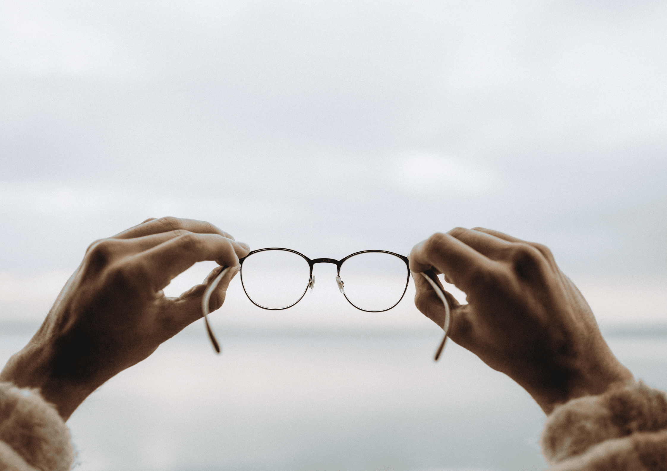 Mãos segurando óculos, sugerindo clareza e alinhamento com os Valores que orientam o comportamento e a cultura da organização
